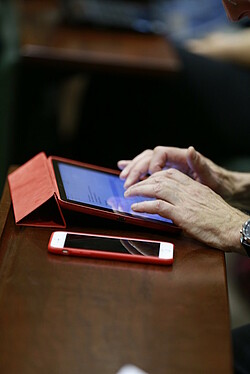 Une personne tape un texte sur une tablette avec un smartphone posé à côté d'elle.